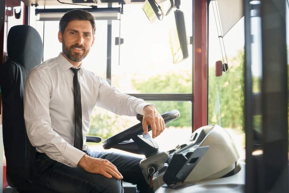 Chauffeur professionnel souriant au volant pour un service de location d’autocar avec chauffeur.