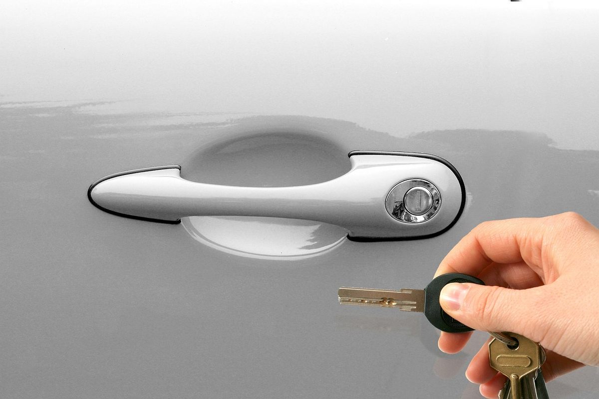 Une main tenant des clés devant une poignée de porte de voiture Une main tenant des clés devant une poignée de porte de voiture