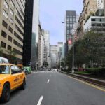 Rue de Manhattan avec taxi jaune stationné, immeubles de hauteur variée et arbres en arrière-plan
