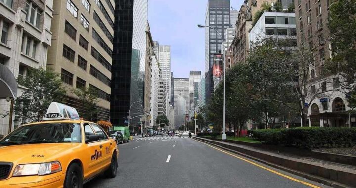 Rue de Manhattan avec taxi jaune stationné, immeubles de hauteur variée et arbres en arrière-plan