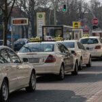 File de taxis blancs garés à une station avec leurs toits illuminés, arbres nus en arrière-plan