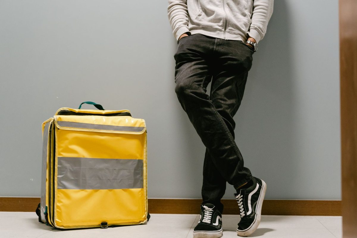 Jeune homme debout à côté d'une valise jaune avec bande réfléchissante contre un mur gris