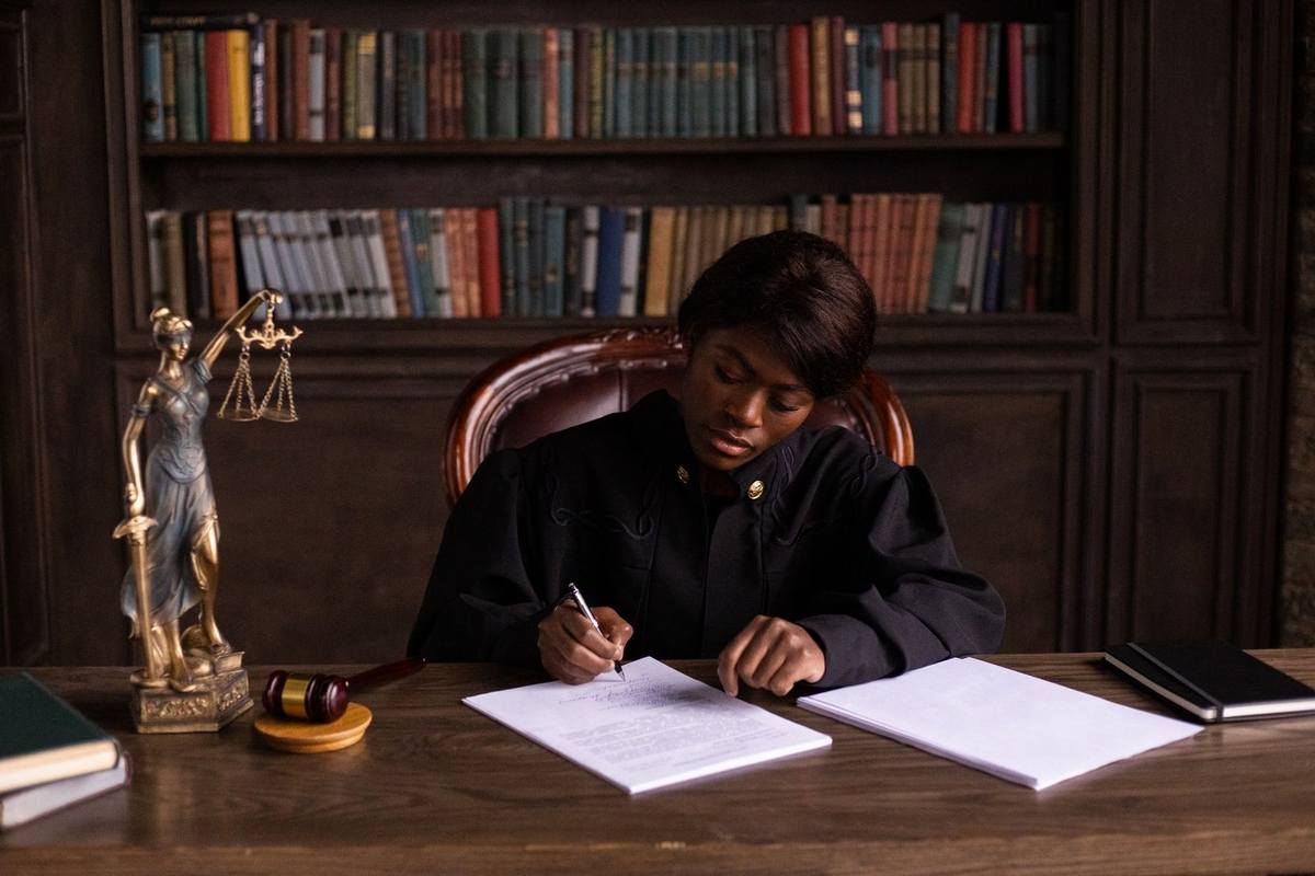 Personne écrivant à un bureau avec des livres, une statue de justice et un gavel en arrière-plan