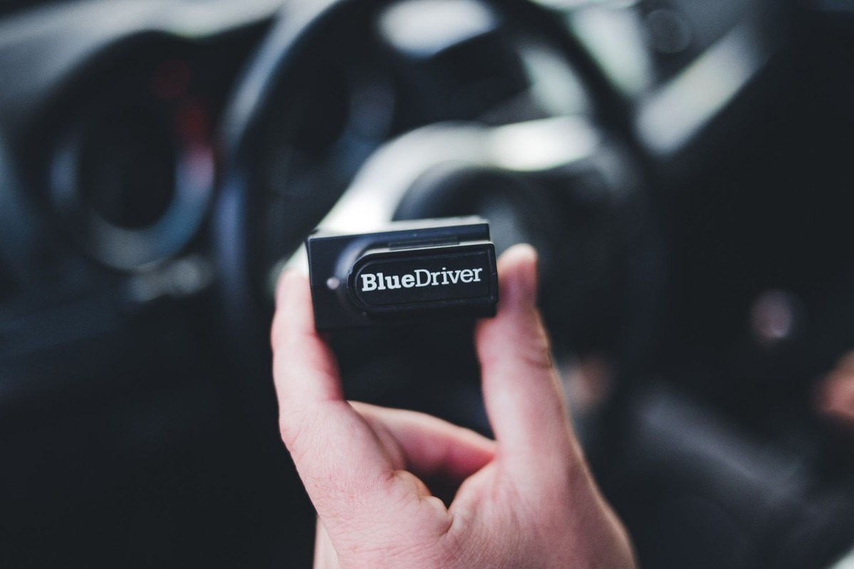 Une main tient un petit boîtier noir à l'intérieur d'une voiture