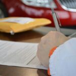 Main tenant un stylo sur un document, enveloppe jaune et voiture rouge en arrière-plan