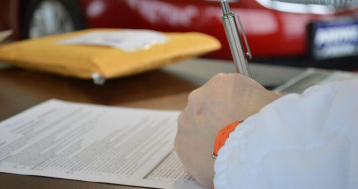 Main tenant un stylo sur un document, enveloppe jaune et voiture rouge en arrière-plan