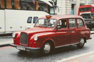 Un taxi rouge circule sur une rue londonienne, entouré de bus et d'un van