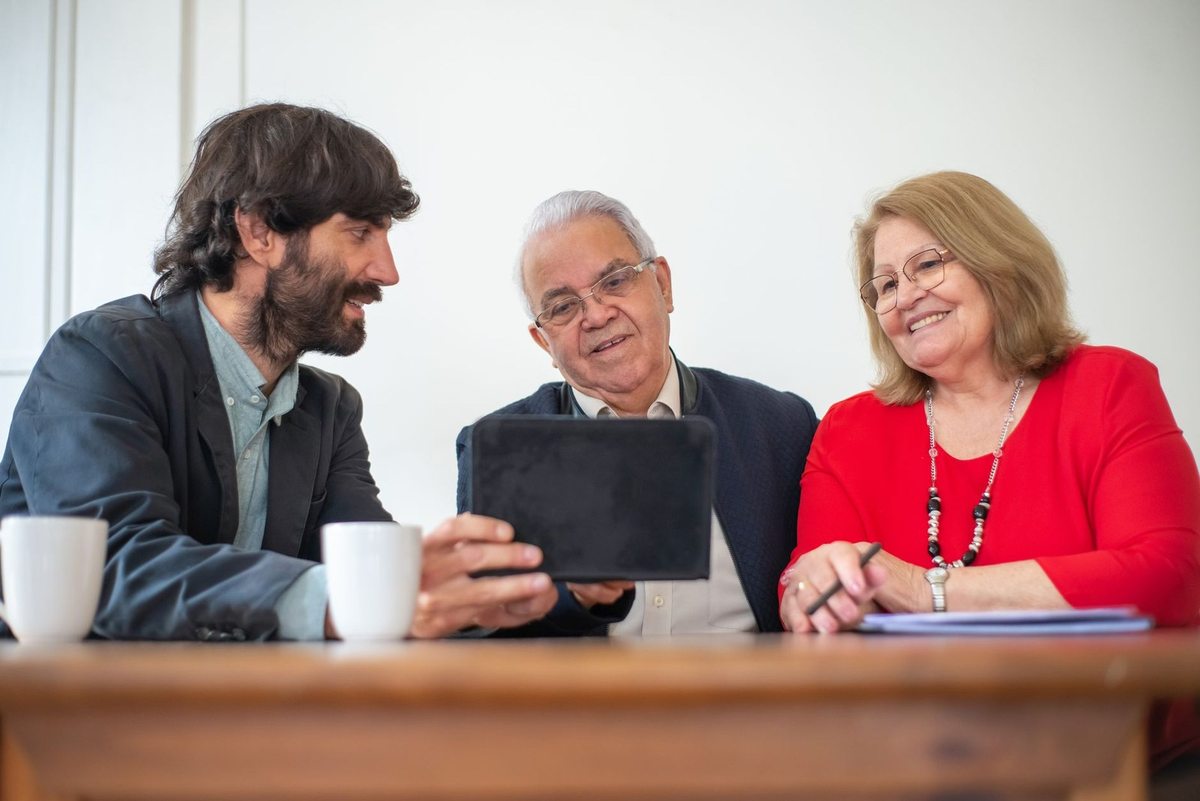 Groupe de trois personnes discutant autour d'une table avec une tablette et des tasses Groupe de trois personnes discutant autour d'une table avec une tablette et des tasses