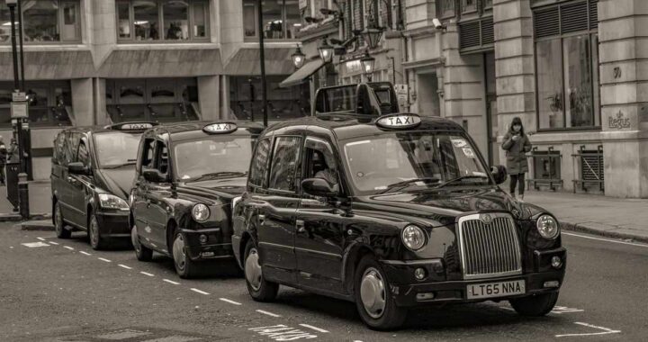 Des taxis noirs en rangée sur une rue de ville, piéton à droite