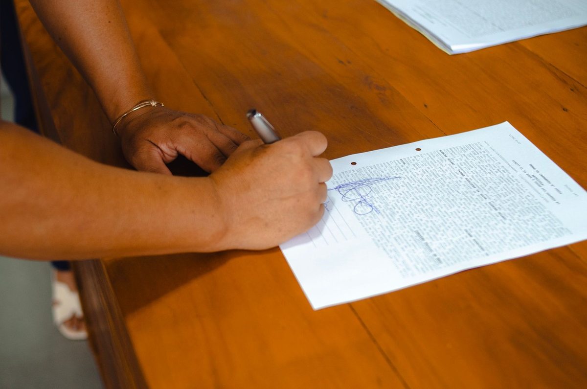 Main droite tenant une plume et écrivant sur un papier posé sur une table en bois Main droite tenant une plume et écrivant sur un papier posé sur une table en bois