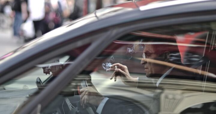 Un homme dans une voiture, main levée, reflet de la rue